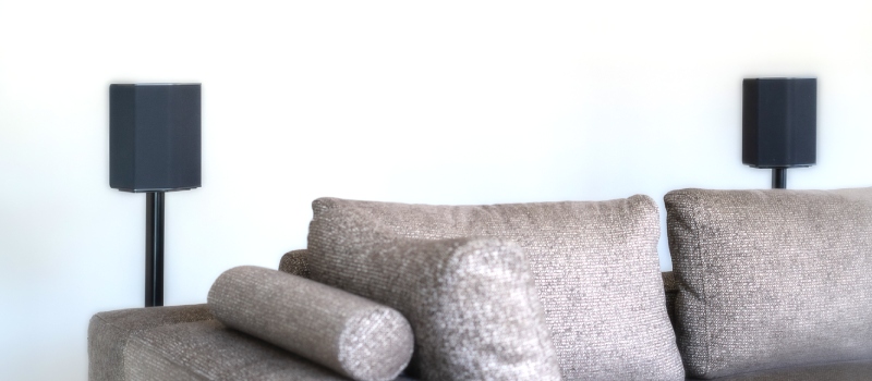 The distance between speakers greatly affects your sound experience. Grey sofa with two black speakers behind it on black speaker stands