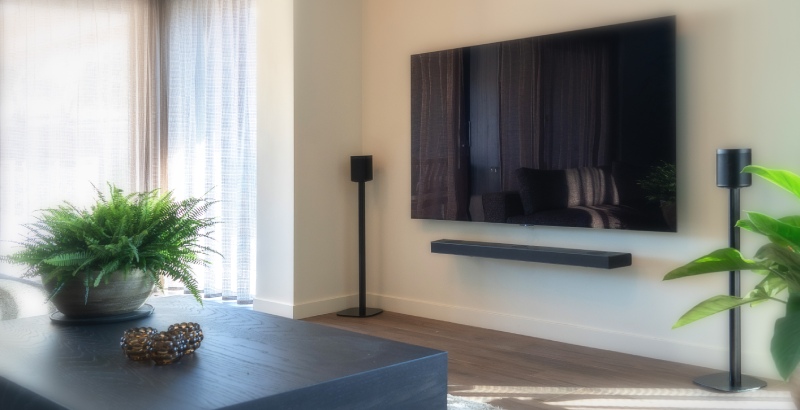 How should you position your speakers? Read all about it here. A television on the wall with two speakers next to it on speaker stands in the living room.