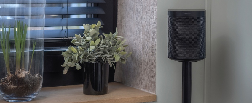 Compact black speaker on a slim stand in the corner of a room